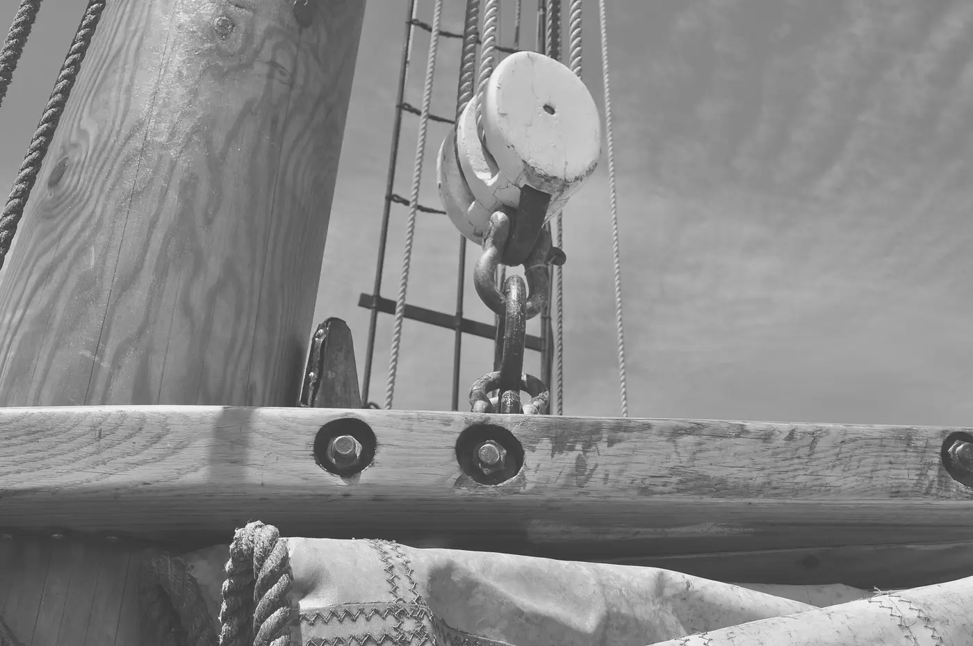 A wooden block and part of a boom, rigged with rope, on the deck of a sailing ship.