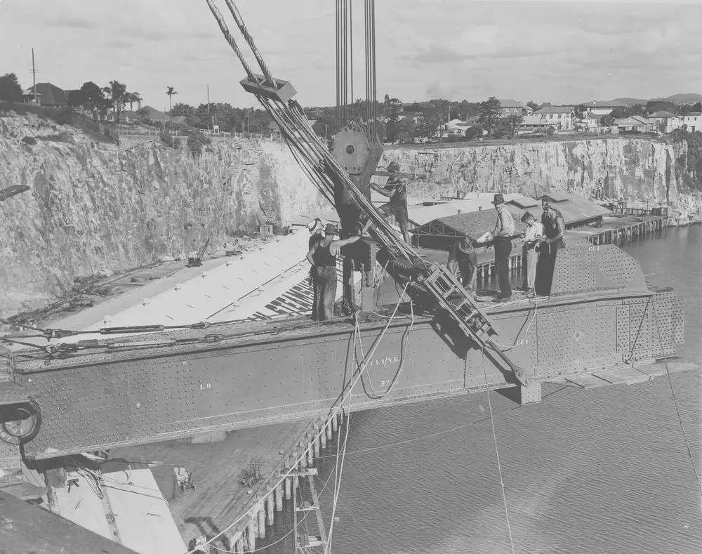 Workers standing on a steel girder suspended from cables during the construction of the Story Bridge, Brisbane, about 1937.